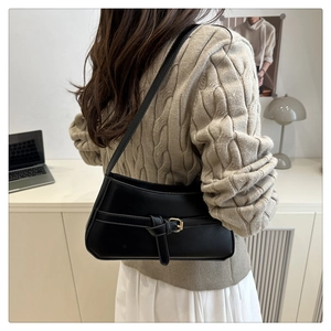 Detail of a minimalist black baguette shoulder bag with gold buckle and knot detail