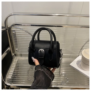Detail of black mini tote bag with silver chain strap on a modern shelf display