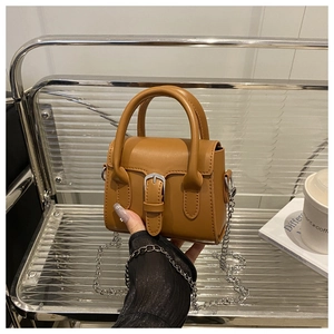 Macro detail of tan leather mini square handbag with silver chain strap and metal clasp
