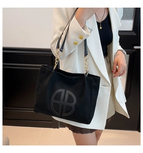 Detail of black tote bag featuring embossed B logo and gold chain shoulder strap