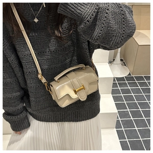 Détail d'un sac bandoulière crème avec boucle H dorée sur un pull en maille gris foncé