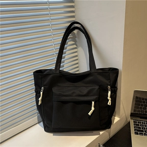 Minimalist black canvas tote bag with front pocket and contrast rope knot detailing