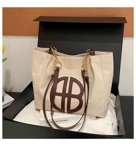 Detail of canvas tote bag with brown leather trim and gold chain inside a luxury gift box