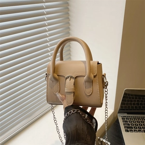 Minimalist beige crossbody square bag with silver chain strap and top handle held by hand