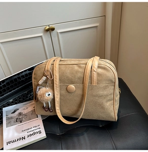 Large khaki suede tote bag with plush pendant on leather chair next to laptop