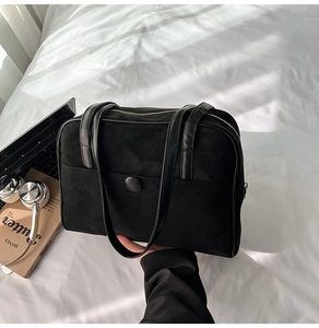 Top view of a large black suede tote bag on white bedding with tech accessories