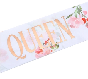 Close-up of a white satin sash with rose gold QUEEN lettering and floral prints