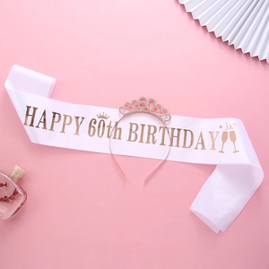 Close-up of a rose gold 60th birthday crown and white satin sash on pink background