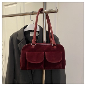 Gros plan d'un sac à main en velours bordeaux avec deux poches avant sur un support