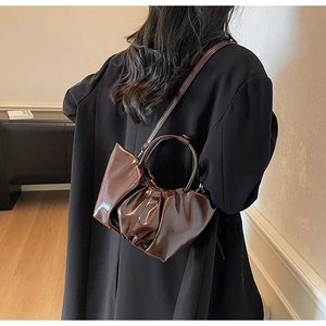Brown patent leather pleated cloud bag shown with model for size and style perspective