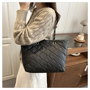 Close-up of black quilted tote bag featuring golden chain strap and rhombus texture