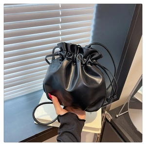 Detail of a minimalist black leather drawstring bucket bag with fine pleated closure