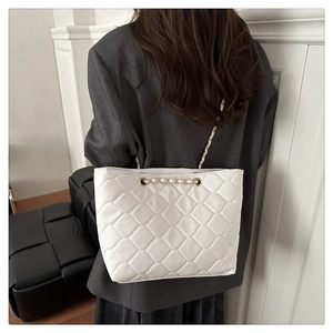 Detail of white quilted faux leather tote bag featuring gold chain strap and stitching