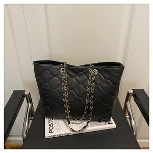 Detailed view of black quilted faux leather handbag with gold chain strap on a chair