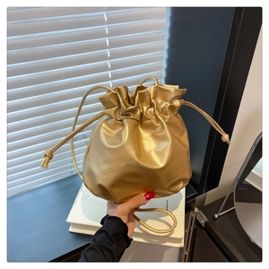 Detail of a golden drawstring bucket bag with soft pleated design and slim shoulder strap