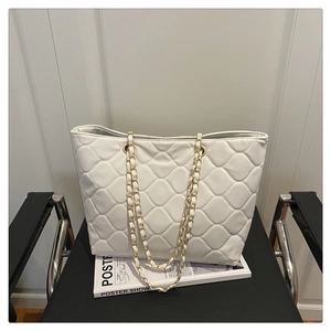 Close-up of white quilted tote bag with elegant chain strap on a designer magazine