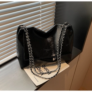 Detail of glossy black patent leather shoulder bag with textured finish and silver chains