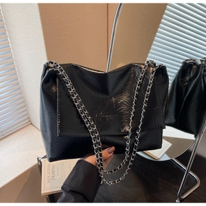 Detail of black glossy pleated shoulder bag with silver chain strap and embossed logo