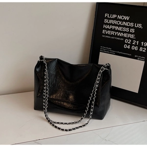 Close-up of black glossy leather shoulder bag with textured wrinkles and silver chain
