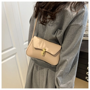 Borsa a tracolla beige minimalista con chiusura dorata indossata da modella in ambiente interno