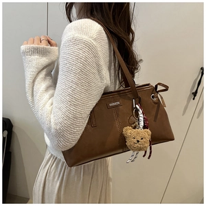 Detail of a brown PU leather tote bag featuring a teddy bear charm and metal fashion logo