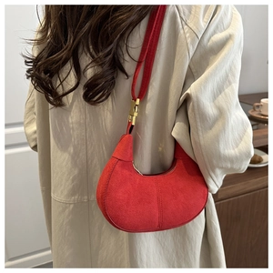 Detail view of red suede crescent bag with gold clasp on a beige trench coat