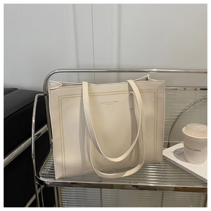Dettaglio della borsa tote beige in pelle con cuciture gialle e logo dorato