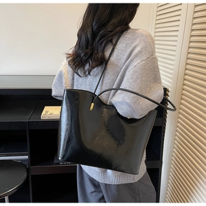 Detail of glossy black patent leather tote bag with elegant golden hardware and wave design