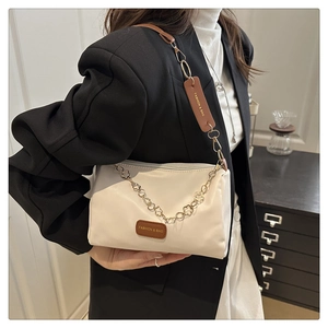 Détail du sac bandoulière blanc avec chaîne à fleurs dorées et étiquette en cuir tendance