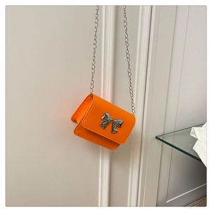 Macro detail of vibrant orange mini bag with silver bow clasp and sleek metal chain strap
