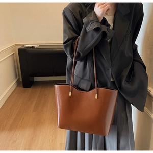 Close-up of brown faux leather tote bag with gold metal hardware on model