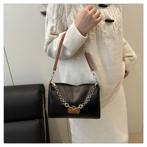Gros plan du sac en cuir noir avec chaîne fleur dorée et détail de sangle brune