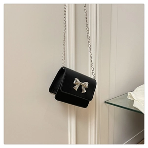 Close-up of a mini black crossbody bag featuring a silver bow buckle and chain strap
