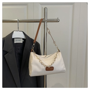 Détail du sac oreiller crème avec chaîne fleurie dorée et écusson logo sur veste