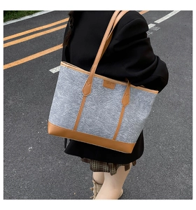Detail of grey felt tote bag with brown leather trim carried by a model on a city street
