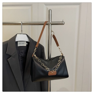 Détail du sac trapèze noir avec chaîne trèfle dorée et étiquette en cuir sur cintre