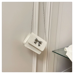 Close-up of a white mini crossbody bag with a silver butterfly bow and metal chain strap