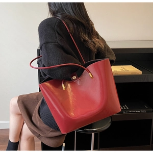 Detail of red glossy leather tote bag with slim shoulder strap and gold buckle accent