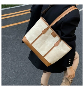 Detail of large canvas tote bag with brown leather trim and shoulder strap on a model