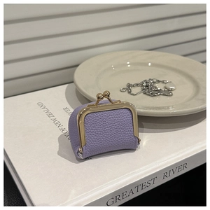 Mini monedero morado con grano de lichi y cierre dorado sobre un libro blanco