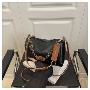 Détail du sac polochon noir en cuir avec chaîne à fleurs dorées et bandoulière marron