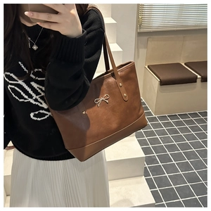 Detailed close-up of brown tote bag showing gold bow buckle and rivet stitching