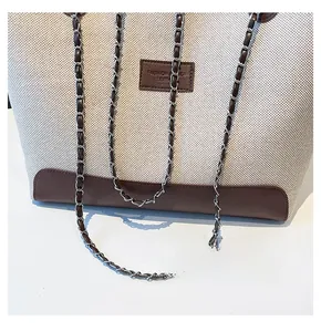 Dettaglio di borsa tote in tela con finiture in pelle marrone e catena in metallo