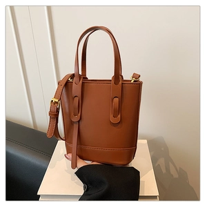 Detailed close-up of brown bucket bag with golden hardware and cylindrical handles