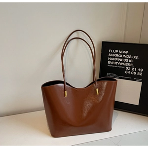 Macro view of polished dark brown leather tote bag showing golden buckles and fine texture