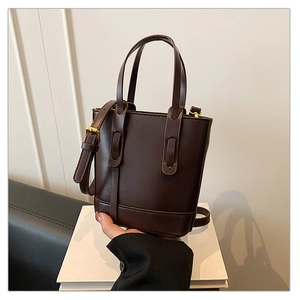 Detail of dark brown leather bucket bag with gold hardware and slim handle on white base