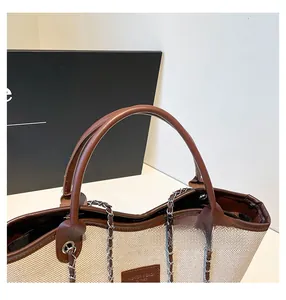 Dettaglio della borsa tote in tessuto con manici in pelle marrone e catene metalliche
