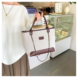 Dettaglio della borsa tote in tela con finiture in pelle marrone e catena in un caffè