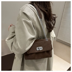 Braune Wildleder-Kettentasche mit Strass-Schnalle an einem Model in minimalistischer Szenerie