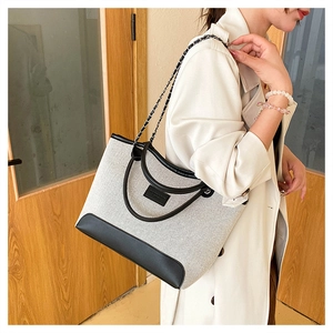 Dettaglio della borsa tote in tela e pelle con tracolla a catena e logo sulla modella